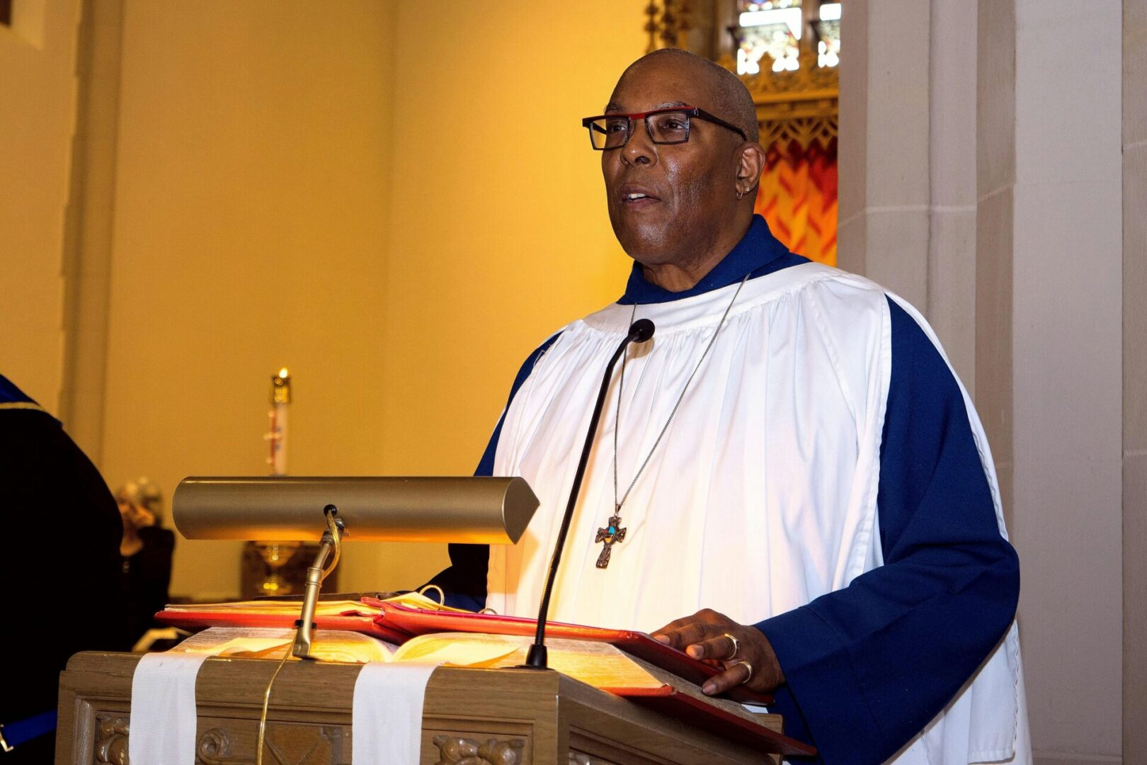 Black man with cross necklace preaching from a pulpit