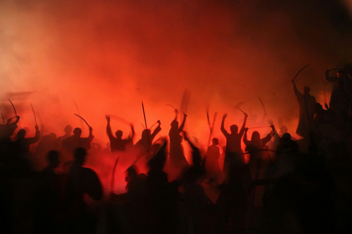 A mass of people holding ancient weapons, with red, foggy background