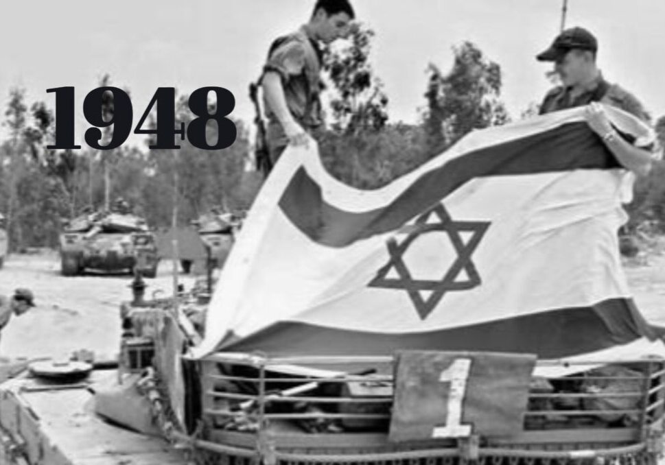 Israeli soldiers standing on tank holding up Israeli flag