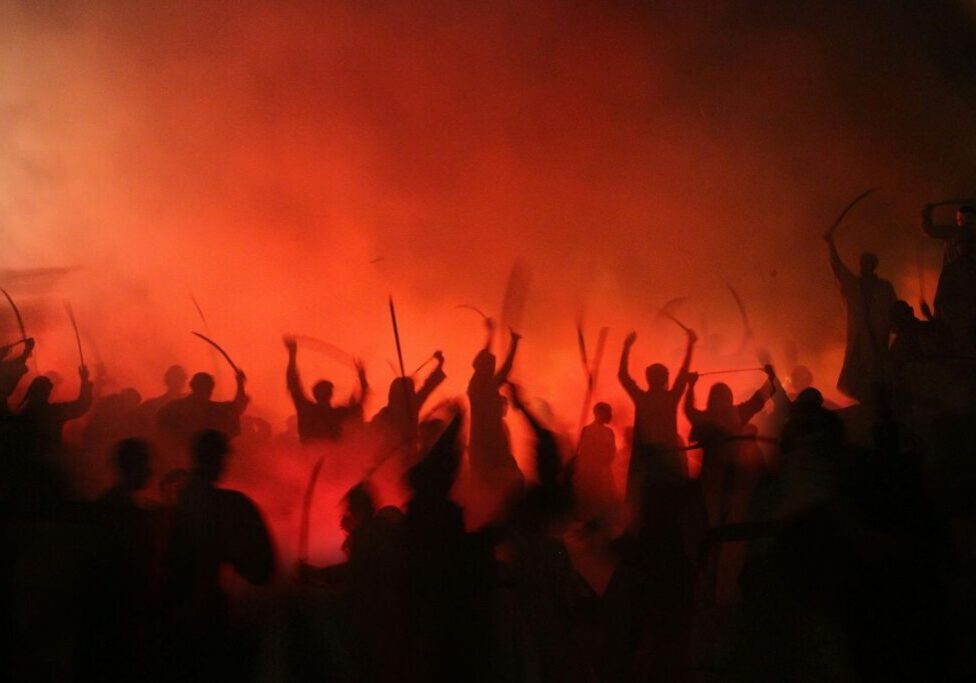 A mass of people holding ancient weapons, with red, foggy background