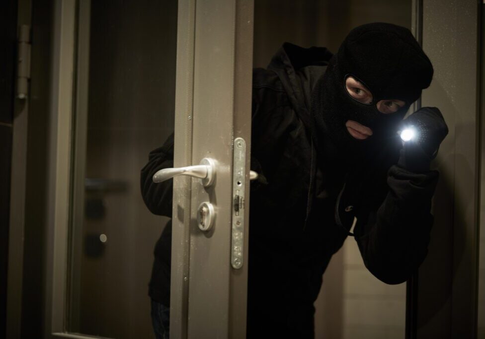 Burglary concept. break-in of an apartment or robbery. Thief in mask opening the door with light.